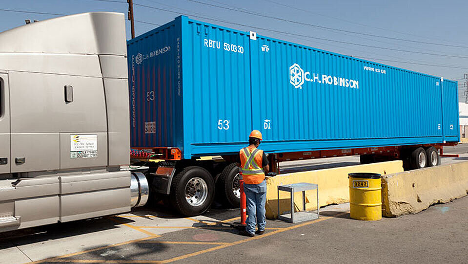 Ein LKW mit einem blauen Container, an dem ein Mann in oranger Warnweste und Helm arbeitet