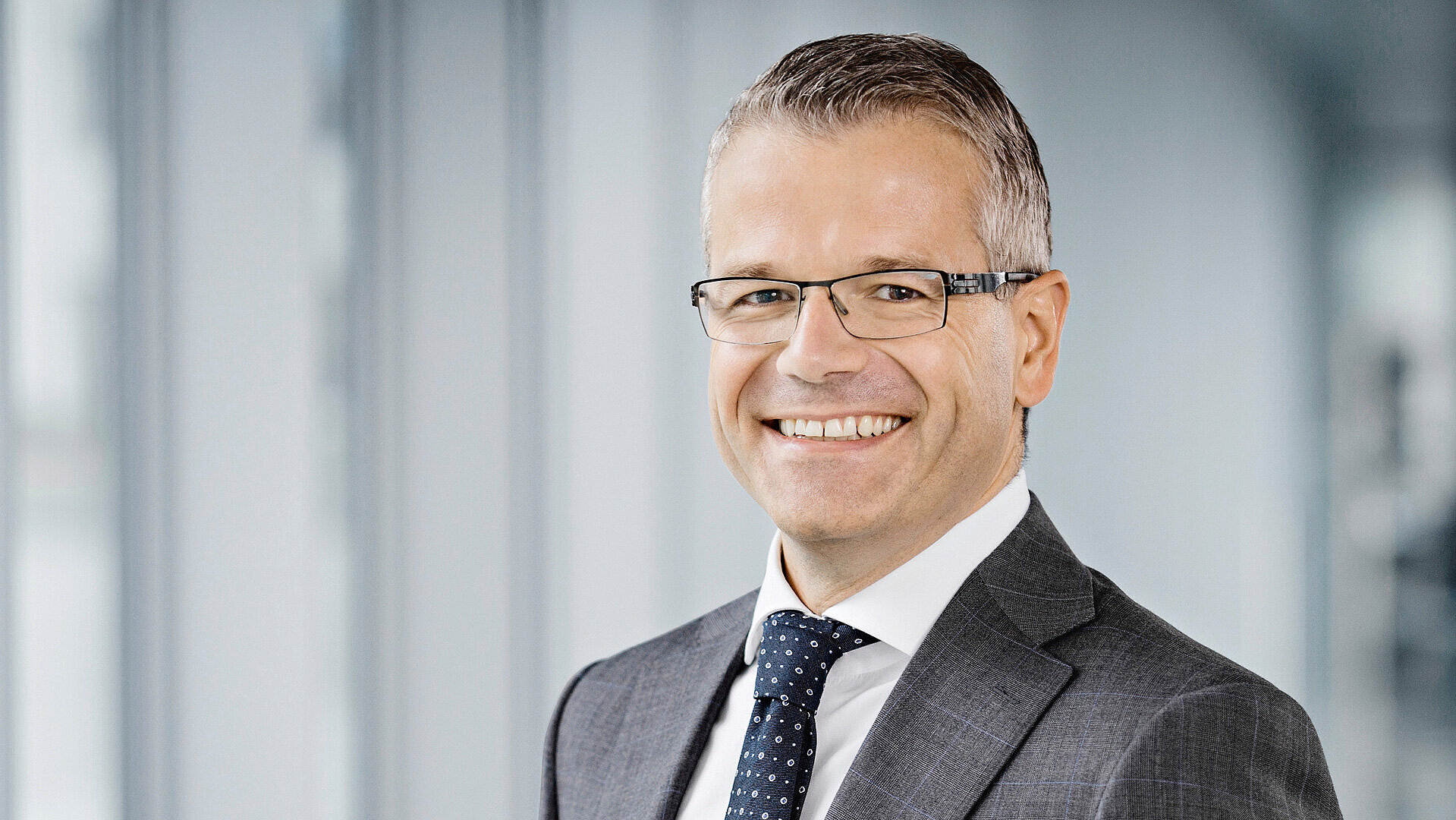 Ein Mann in einem Anzug und mit Brille lächelt in die Kamera