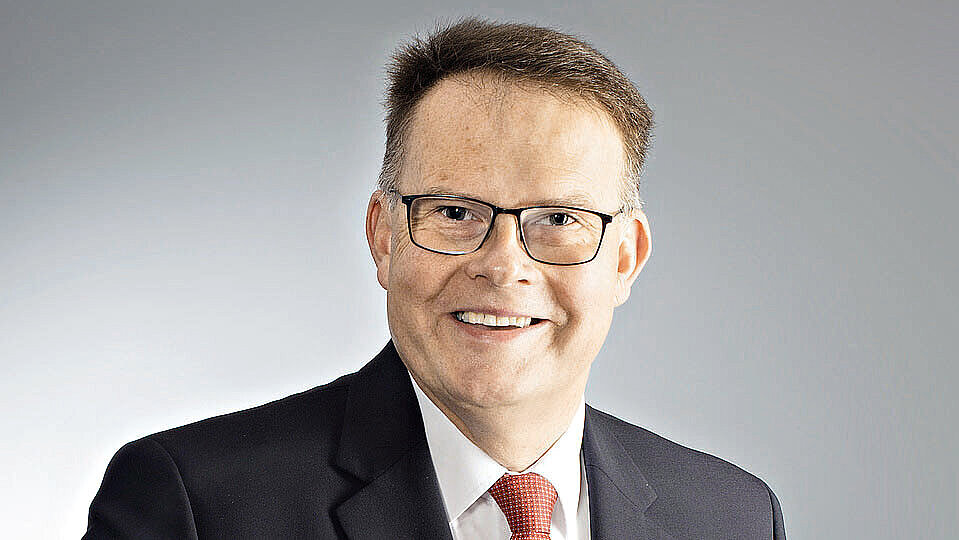 Ein Mann in einem Anzug und einer roten Krawatte lächelt in die Kamera