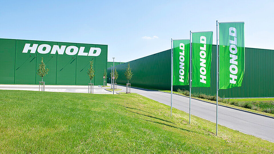 Ein großes grünes Gebäude mit der Aufschrift Honold und davor vier grüne Banner